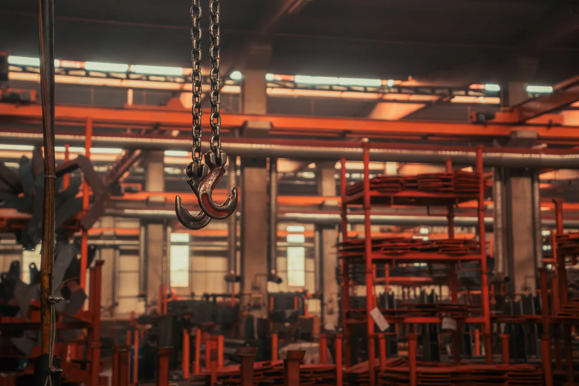Industrial warehouse interior with overhead crane hooks and stacked metalwork